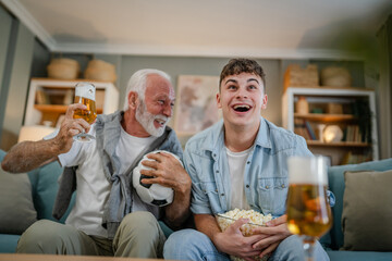 teenager and his grandfather senior man watch football game at home