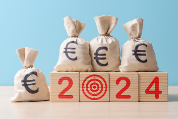 Moneybags with Euro symbols on wooden blocks with digits 2024. Concept of 2024 business and financial goals