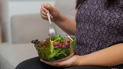 Overweight woman enjoy eating a bowl of vegetable salad at her home