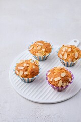 Curd muffins sprinkled with almond petals in paper molds on a ceramic board on a white concrete background.