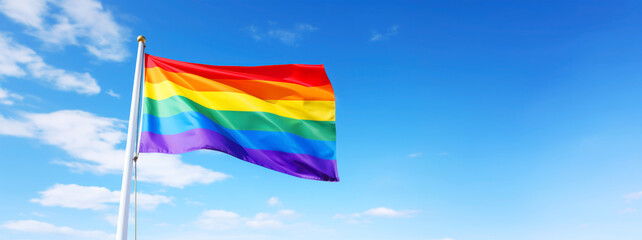 LGBT rainbow flag on flagpole fluttering in the wind against clear blue sky