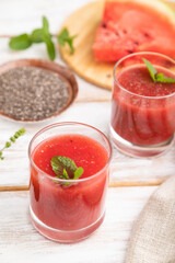 Watermelon juice with chia seeds and mint in glass on a white wooden background with linen textile. Side view, selective focus.