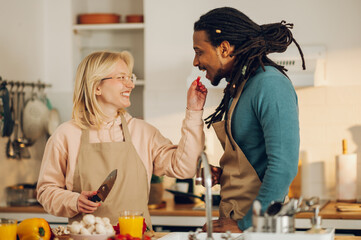 A cheerful wife is cooking and feeding her Arabic husband.