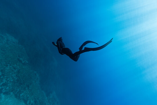 Freediver Swimming in Deep Sea With Sunrays. Young Man DIver Eploring Sea Life.