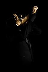 Man dressed in black suit holding gold objects on black background