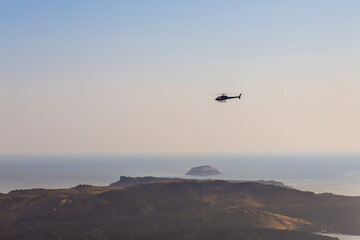 Helicopter flying over the volcanic Santorini island on a sunset sky