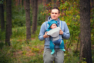 Young father with his newborn baby in a sling walking in the autumn forest. The concept of a happy...