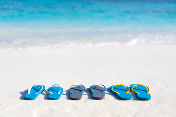 Obraz premium Three pairs of flip flops on the beach on the background of ocean in the Maldives. Family vacation