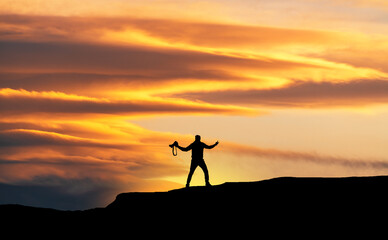 Silhouette of the hiker on the hill at the sunset.