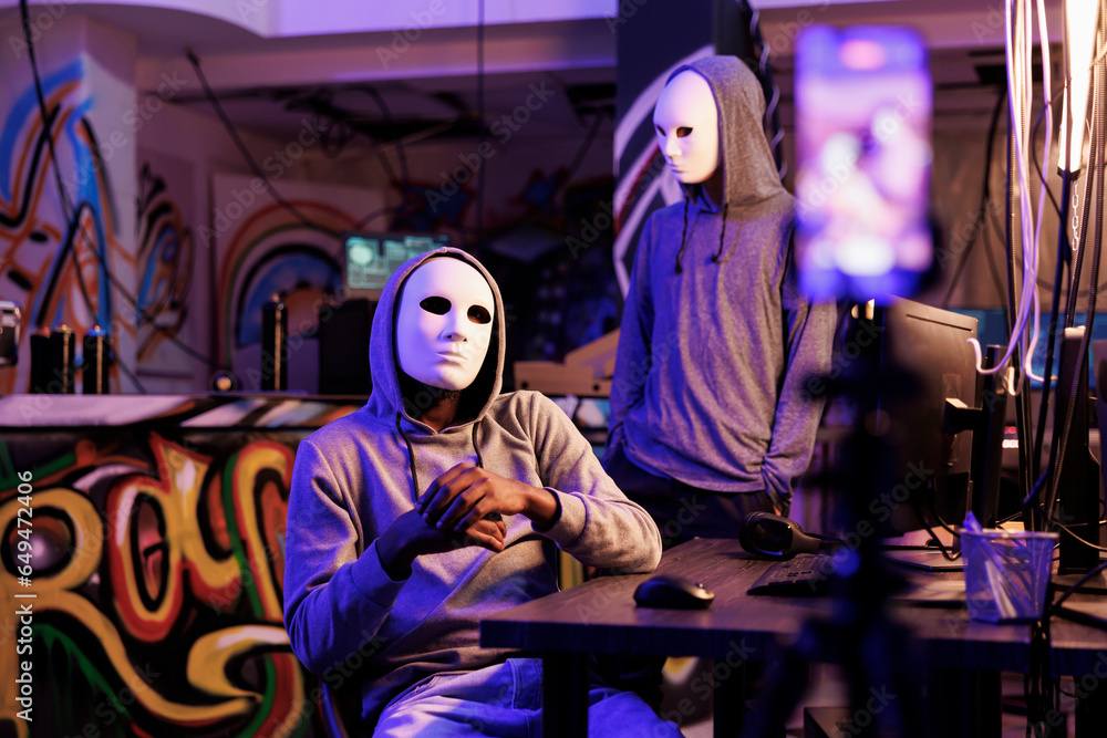 Poster scammers recording illegal activities on smartphone in abandoned warehouse. anonymous internet thiev