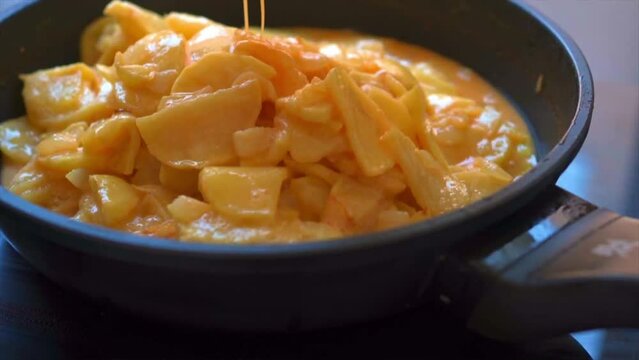 Chef mixing fried potatoes with eggs to make a Spanish omelette (tortilla de patatas)
