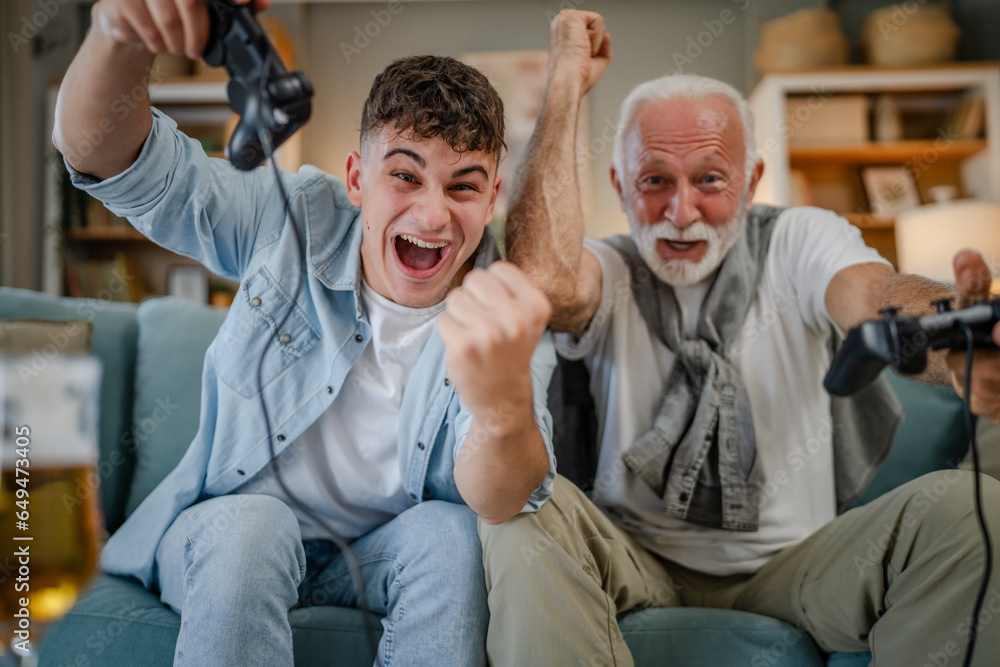 Wall mural teenager male and his grandfather senior man play console video game