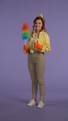 Vertical photo. Woman in casual clothing and rubber gloves holding pipiduster, showing thumbs up at the camera, smiling face expression.