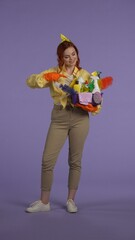 Vertical photo. Woman in casual clothing and rubber gloves smiling face holding basket with cleansers, pointing.