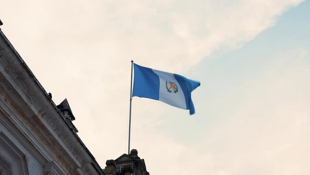 Bandera nacional de Guatemala ondeando en Centroam&eacute;rica al viento sobre asta en un edificio en palacio de gobierno mostrando respeto y patriotismo 