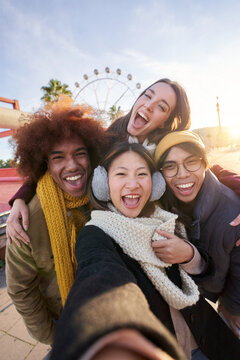 Vertical Excited Smiling Group Multiracial Friends Taking Funny Selfie Looking At Camera Standing Together Outdoor. Multi-ethnic Young People In Amusement Park Having Fun In Sunny Winter Holiday. 