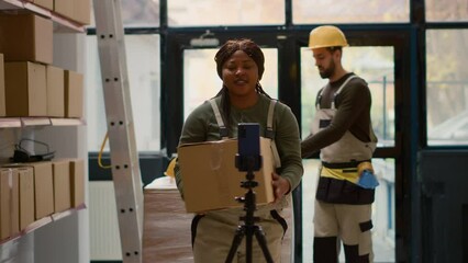 Warehouse supervisor pressing play on cellphone placed on tripod to start recording training video for interns. Quality assurance manager filming tutorial showing trainees how to arrange parcels