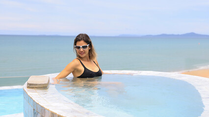 Young woman relax on the edge of the rooftop swimming pool of the hotel against the beautiful sea background
