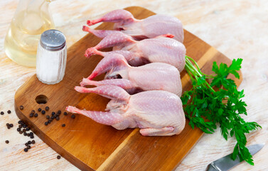 Uncooked quails on wooden board with parsley and black pepper. Home kitchen, preparing food.