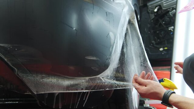 Process of applying a protective PPF film to a car. Hands of a professional applying a protective film. Closeup shot view