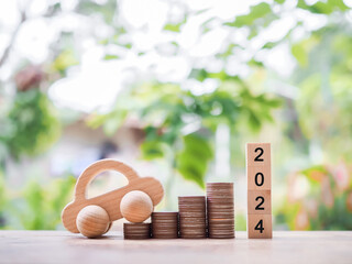 Wooden block with number 2024 and wooden toy car on stack of coins. The concept of saving money  for car in new year 2024