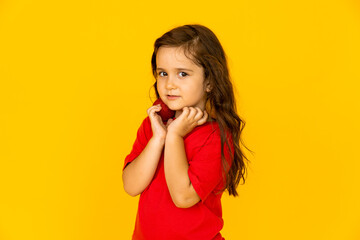 A cute little girl in a red t-shirt holding Christmas tree toys. yellow background, space for text