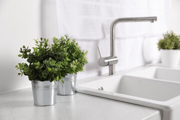 Artificial potted herbs on white marble countertop near sink in kitchen. Home decor