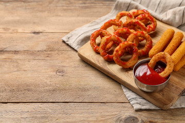 Tasty fried onion rings, cheese sticks and ketchup on wooden table, space for text