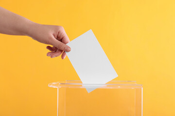 Woman putting her vote into ballot box on orange background, closeup