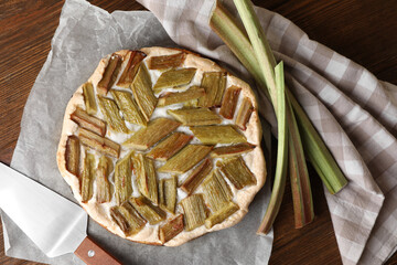 Freshly baked rhubarb pie, stalks and spatula on wooden table, flat lay