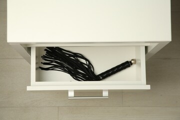 Black whip in drawer indoors, top view. Sex toy