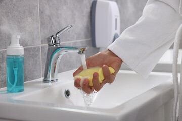 Young man cleaning face sponge above sink in bathroom, closeup