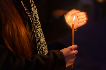 A candle in the hands of a praying woman. Symbolic concept. Background with selective focus - obrazy, fototapety, plakaty