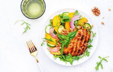 Delicious healthy salad with peaches, grilled chicken breast, cucumber, walnuts, red onion, green basil and mixed herbs, white table background, top view
