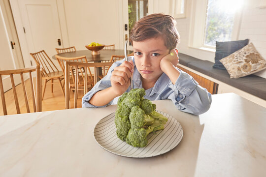 Displeased boy (8-9) looking at broccoli on plate in kitchen