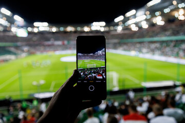 Fan hand with smartphone photographing football match. Using mobile phone camera at the stadium.