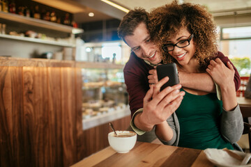 Young interracial couple using a smartphone and drinking coffee in a cafe while on a date