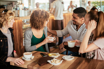 Young and diverse group of friends having a conversation over some coffee and desserts in a cafe