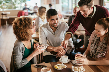 Young and diverse group of friends having a conversation over some coffee and desserts in a cafe