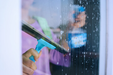 Woman cleaning window with squeegee and spray detergent bottle at home
