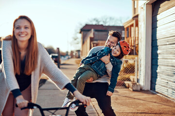 Young Caucasian family walking and riding a bicycle on a sidewalk in the suburbs of a city