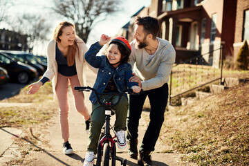 Young Caucasian family teaching their son to ride a bike in the suburbs