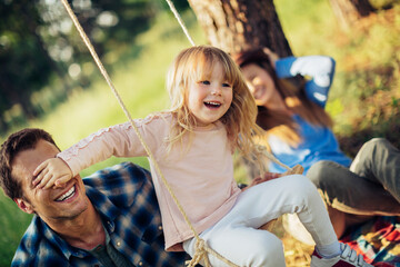 Young Caucasian family playing on a swing while on a picnic in the park