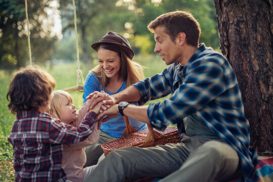 Young Caucasian family holding hands while having a picnic in the park