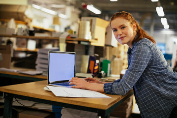 Portrait of a young Caucasian woman working on the laptop in a printing press office