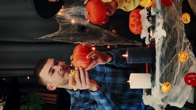 Happy couple friends painting orange pumpkins at Halloween party. Vertical video