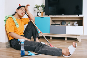 Young Asian woman sitting on floor feeling tired after doing housework.  - obrazy, fototapety, plakaty