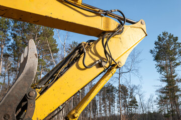 The boom arm elbow and hydraulics tubing on a working heavy equipment excavator on a new home construction site, with blue sky and trees in the background.