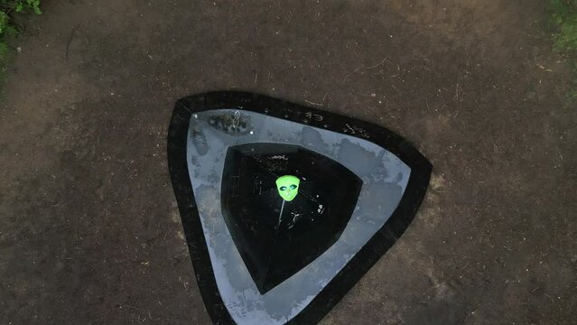 Rising aerial view looking down over funny alien mask laid on Rendlesham forest flying saucer landing sire