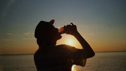Traveler woman silhouette drinking beer from tin can lit by sunset beams overlooking sea. Alcohol relaxation in vacation.